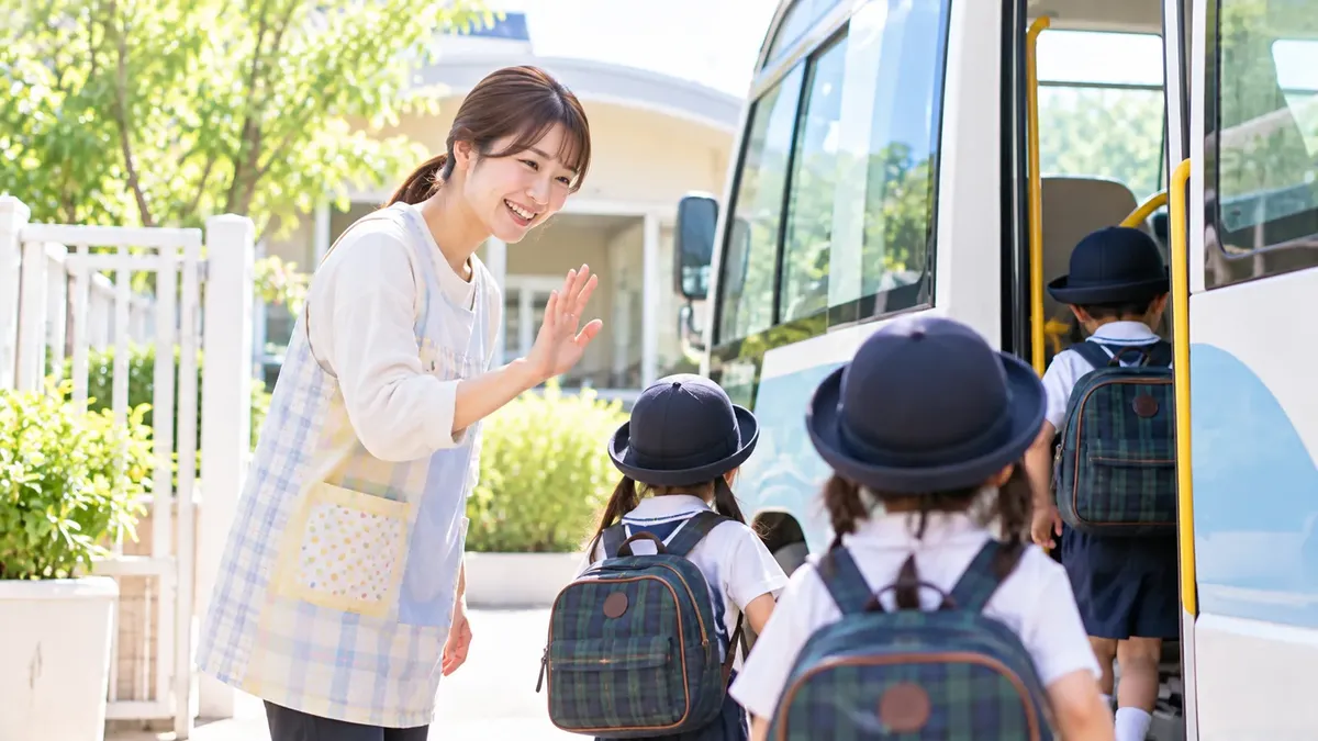 園バスの前で、先生が帽子をかぶった子どもたちを迎えている
